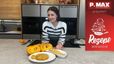 Sarah lächelnde, steht in einer modernen Küche und präsentiert einen fertigen Kürbis-Cheesecake mit Streuseln. Vor ihr auf der Arbeitsplatte liegen die Zutaten, darunter ein aufgeschnittener Kürbis, sowie der angerichtete Kuchen auf einem Teller.