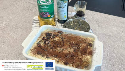 Kernöl-Tiramisu in einer weißen Auflaufform, garniert mit Kakaopulver und karamellisierten Käferbohnen für den besonderen Crunch. Im Hintergrund sind die regionalen Hauptzutaten angerichtet: eine Flasche steirisches Kürbiskernöl, eine Dose Käferbohnen sowie eine Schale mit Kürbiskernen.