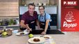 Philipp und Peter Lehner stehen lächelnd in einer modernen Küche und präsentieren das fertige Gericht. Vor ihnen auf der Arbeitsfläche stehen mehrere Teller mit frisch zubereitetem Beef Tatar, das jeweils mit einem Eigelb garniert ist. Einer der Männer deutet einladend auf den vordersten Teller.