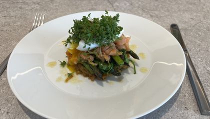 Ein knuspriger Rösti, belegt mit grünem Spargel, Räucherlachs und einem pochierten Ei. Das Gericht ist mit frischer Kresse garniert und auf einem weißen Teller angerichtet.
