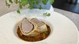 Zwei Scheiben Schweinsfilet im goldbraunen Strudelteig, angerichtet auf einem herzhaften Bohnen-Cassoulet mit weißen und Kidneybohnen. Das Gericht wird in einer weißen, strukturierten Schüssel serviert, im Hintergrund ist eine grüne Kräuterpflanze erkennbar.