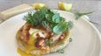 Ein goldbraun gebratenes, knuspriges Flatbread auf einem weißen Teller, belegt mit Räucherlachs und einem pochierten Ei, dessen flüssiges Eigelb über den Rand läuft. Das Gericht ist reichhaltig mit frischen grünen Kräutern wie Dill und Minze garniert und mit rotem Tomatenöl beträufelt.