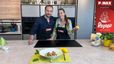 Max Impertro und Tanja stehen lächelnd nebeneinander in einer modernen Küche hinter einer Kochinsel. Im Vordergrund ist ein fertig angerichteter Teller mit Tortellini und einer Garnele auf einem hellgrünen Platzset zu sehen. Tanja hält eine Zitrone in der Hand, während im Hintergrund Backzutaten bereitstehen.