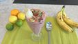 Ein hohes Glas gefüllt mit rosafarbener Nicecream, die mit einem Bananenstück, einer Erdbeere, Minze, Cookie-Dough-Stückchen und Schokoraspeln garniert ist. Daneben liegen frische Bananen und verschiedene Zitrusfrüchte auf einer hellgrünen Unterlage.