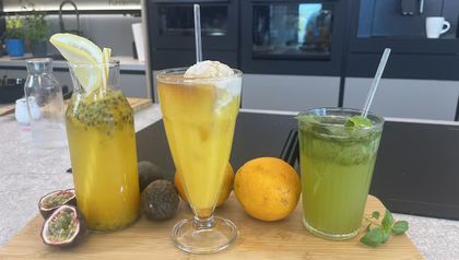 Die drei im Rezept beschriebenen Sommerdrinks auf einem Holzbrett angerichtet: links die Maracuja-Limonade in einer Glasflasche, in der Mitte der „Sanfte Engel“ mit Vanilleeis und Espresso und rechts die grüne Basilikum-Limonade.