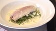 Ein pochiertes Forellenfilet, angerichtet in einer weißen Schüssel auf einem Bett aus Lauch-Romanasalat. Das Gericht ist mit selbstgemachtem Frischkäse bestreut und mit einer hellen, cremigen Molke-Sauce übergossen.