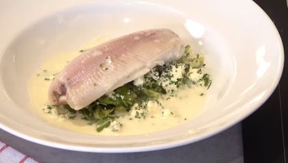 Ein pochiertes Forellenfilet, angerichtet in einer weißen Schüssel auf einem Bett aus Lauch-Romanasalat. Das Gericht ist mit selbstgemachtem Frischkäse bestreut und mit einer hellen, cremigen Molke-Sauce übergossen.