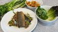 Fertig angerichteter Teller mit gebratenem Saibling auf Gemüse und Sherry-Sauce. Im Hintergrund sind einige der frischen Zutaten für das Rezept zu sehen: Pilze, Romanasalat und Stangensellerie.